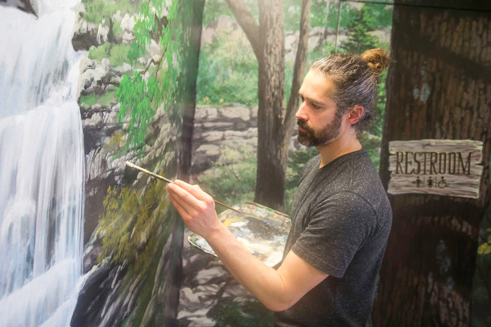 Artist Aaron Wolken finishes an outdoor-themed mural in the pool room.