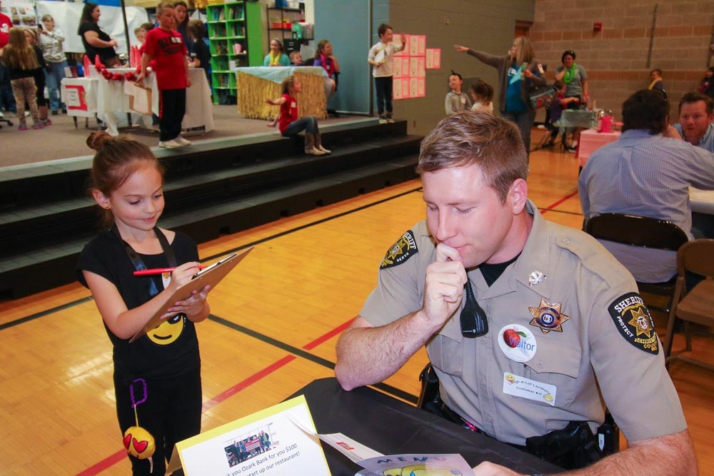 LUNCH BREAK
Above, Ozark East second-grader Riley Murphy takes School Resource Officer Mitchell Null’s order at a restaurant hosted by the school. The culmination of an economics unit, students learned about running a business from local bankers and a former McDonald’s franchise owner before running the restaurant April 18.